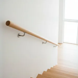 Main courante ronde en hêtre clair sur mesure, posée avec des supports en inox dans un escalier moderne et lumineux.