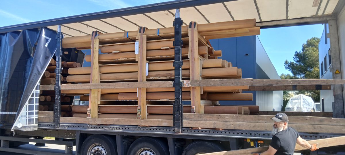 Chargement de rondins de bois massif dans un camion pour l’expédition, avec un opérateur manipulant les pièces près de l’atelier.