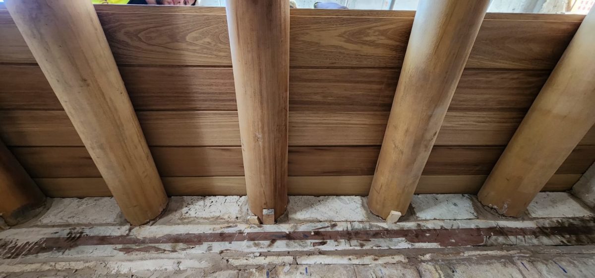 Vue intérieure d’une charpente en bois rond massif posée sur des murs en pierre, illustrant l’usage structurel des rondins