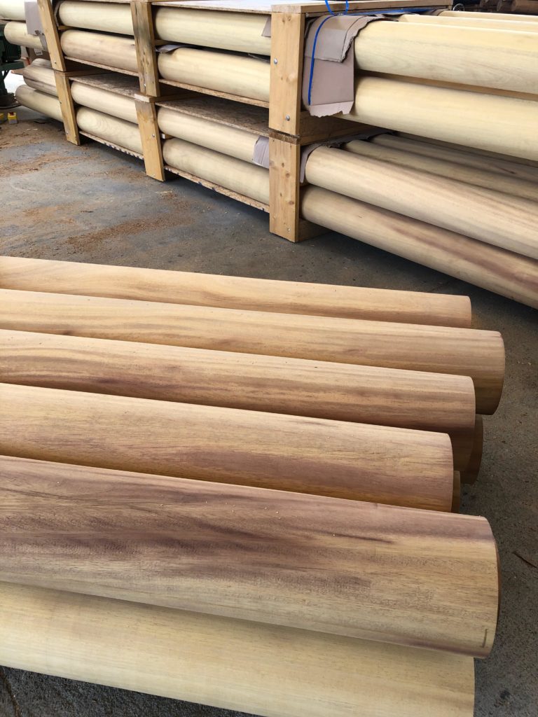 Rondins de bois massif soigneusement préparés et empilés en attente d’expédition dans un atelier, illustrant la qualité de finition et la diversité des teintes naturelles.