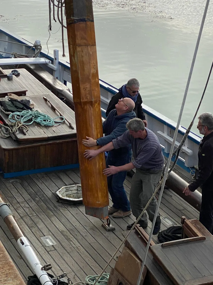 Équipe de marins guidant à la main la mise en place d'un mât en bois lamellé collé WoodSpars sur le pont d'un vieux gréement
