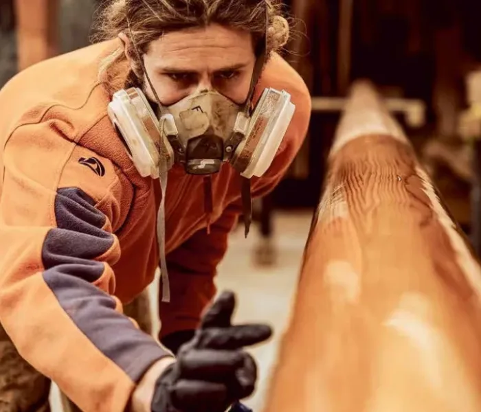 Artisan WoodSpars appliquant un vernis de finition sur un mât en bois lamellé collé dans l'atelier de Locmariaquer