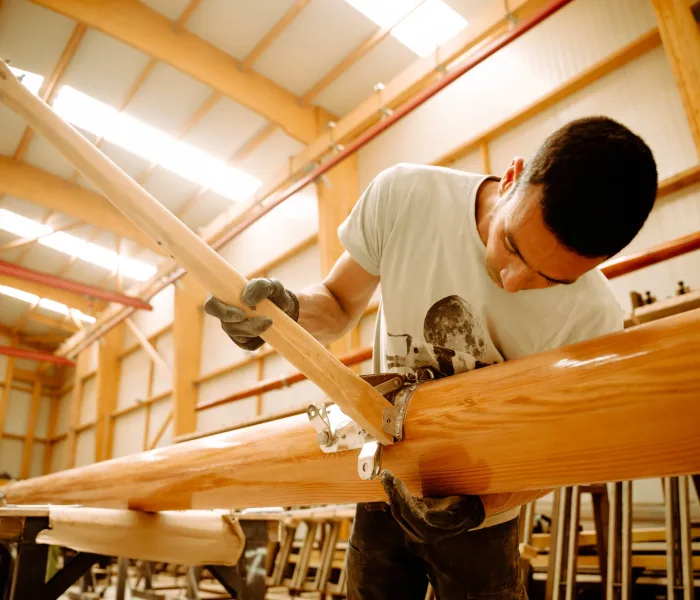 Artisan WoodSpars assemblant des espars en bois à l'aide de serre-joints dans un vaste atelier lumineux de charpente maritime