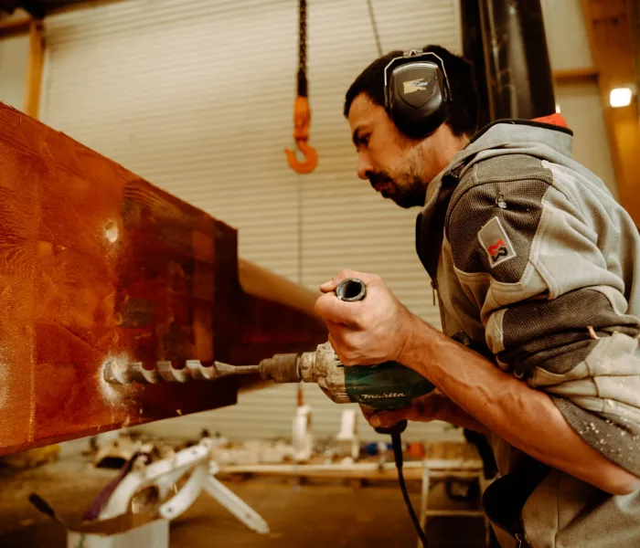 Artisan WoodSpars perçant un epar en bois massif à la perceuse Makita dans l'atelier, protections auditives sur les oreilles